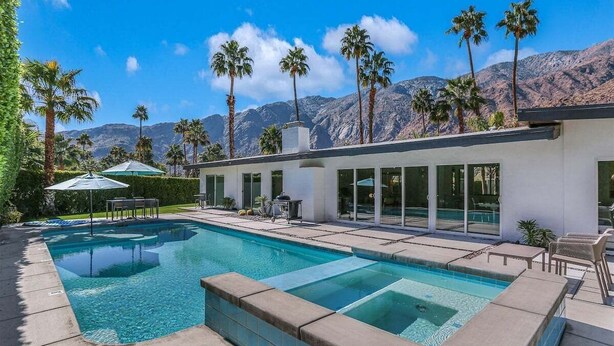 A modern pool area with clear blue water, surrounded by palm trees and mountains in the background. - Las Palmas Alexander – 1962 Alexander Home with Saltwater Pool, Spa, Fire Pit & Mountain Views (Palm Springs)