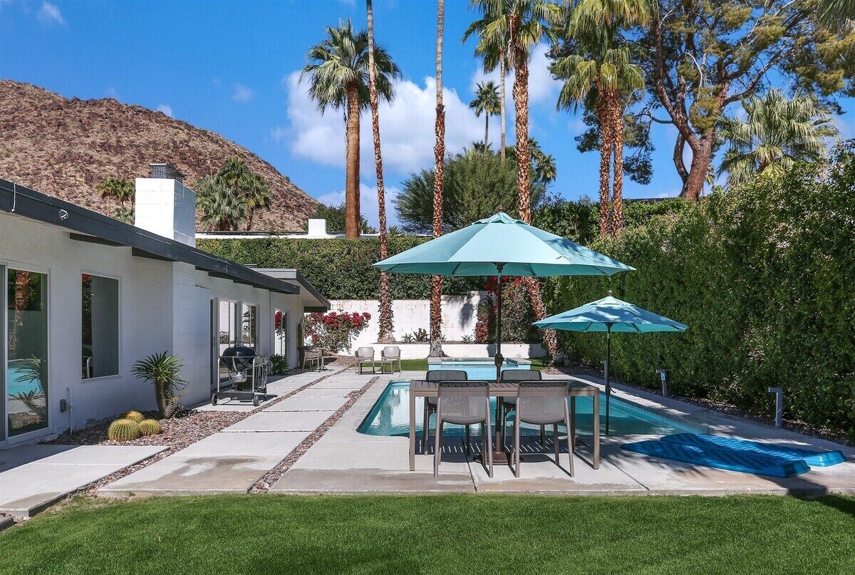 Una casa moderna con piscina, mobiliario de patio y montañas al fondo.