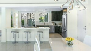 A modern kitchen with a central island, bar stools, stainless steel appliances, and a decorative ceiling light. - Las Palmas Alexander – 1962 Alexander Home with Saltwater Pool, Spa, Fire Pit & Mountain Views (Palm Springs)