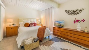 Una camera da letto con un letto, comodini, una TV, un elemento decorativo a parete e un vaso con fiori.