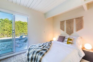 A bedroom with a large bed, a sliding glass door to a balcony, and macrame wall art. - The Elrod - Exclusive Vacation Home with Pool & Spa (Palm Springs)