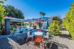 An outdoor patio with a round table and chairs, surrounded by gravel and plants. - The Elrod - Exclusive Vacation Home with Pool & Spa (Palm Springs)