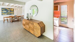Un interno moderno con una scrivania reception in legno, uno specchio rotondo e una sala da pranzo con sedie e tavolo.