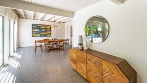 Un'area pranzo moderna con un tavolo e sedie in legno, un grande dipinto astratto sulla parete e uno specchio rotondo sopra una consolle in legno.