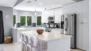 Une cuisine moderne avec des meubles blancs, des appareils en acier inoxydable et un grand îlot central doté de tabourets de bar.