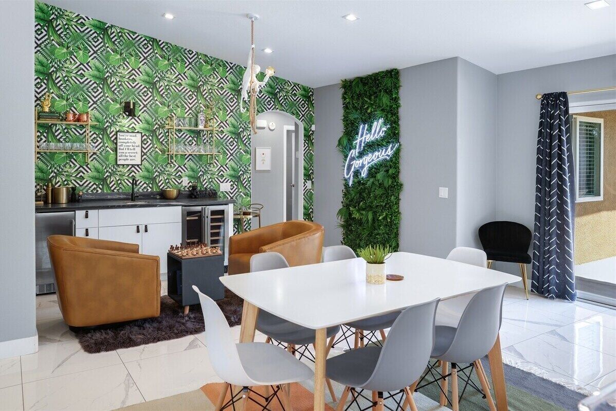 A modern kitchen with a geometric patterned backsplash, a dining area with a white table and grey chairs, and a vertical garden with a neon sign.