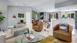 Un salon moderne avec un canapé, des fauteuils et une table basse. Il y a également un coin cuisine équipé d’un réfrigérateur et d’une table à manger.