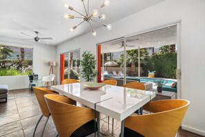 Ein moderner Essbereich mit einem Glastisch, Holzstühlen und Blick auf einen Pool und Grünflächen.
