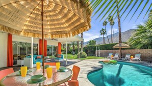 Un espace aménagé au bord de la piscine, avec une table, des chaises et un grand parasol.