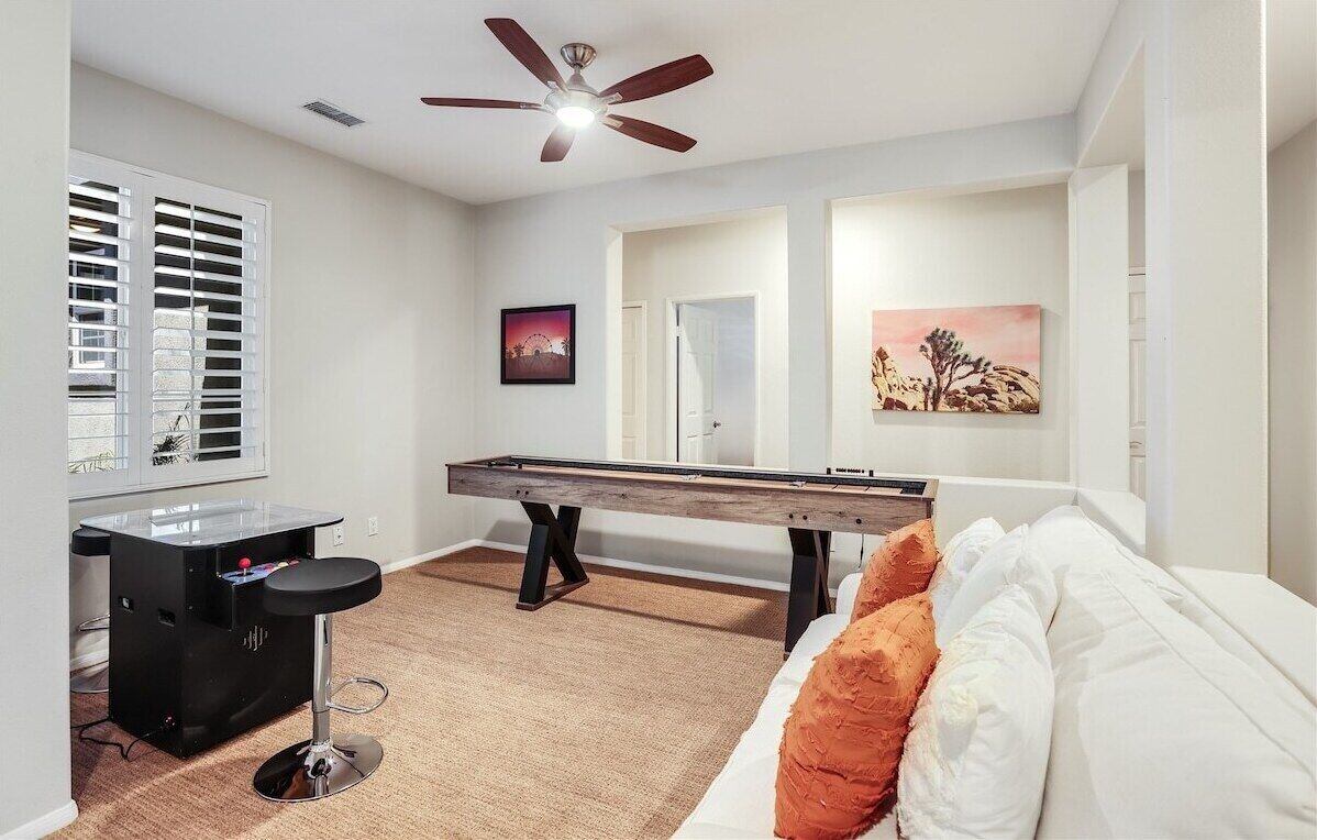 A pool table in a room with a ceiling fan, a bar area, and a bed with pillows.