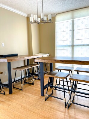 A room with wooden tables and chairs, a ceiling light fixture, and a window with blinds.