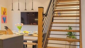 A modern kitchen with a central island, pendant lighting, and a wooden staircase. - Escape 2 Unwind At The Parade, Accommodates 10 (York)