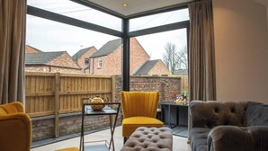 A modern living room with a large glass wall, a wooden fence, and a view of houses. - Escape 2 Unwind At The Parade, Accommodates 10 (York)