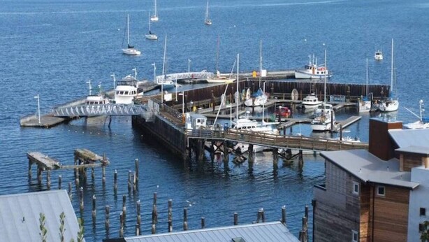 A marina with boats docked, a pier extending into the water, and buildings in the foreground. - Whidbey Island Orchard House Estate Langley, WA (Langley)
