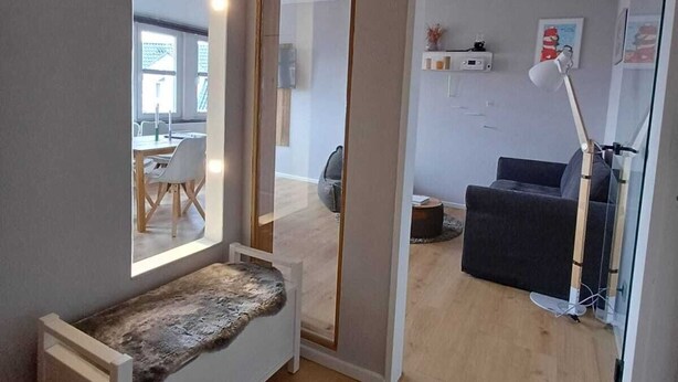 A modern living room with a wooden bench, a large mirror, and a glass door leading to another room. - Seagull's nest in the Villa Medici (Norderney)