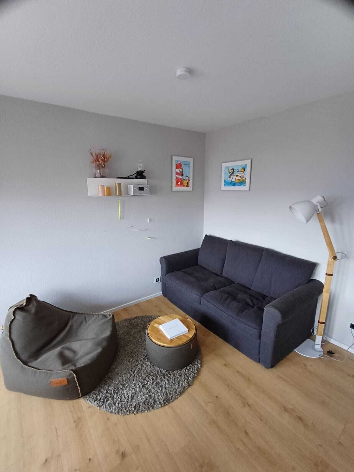 A modern living room with a dark grey sofa, a round wooden coffee table, a grey bean bag chair, and a floor lamp.