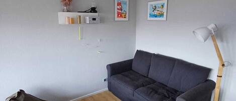 A modern living room with a dark grey sofa, a round wooden coffee table, a grey bean bag chair, and a floor lamp.