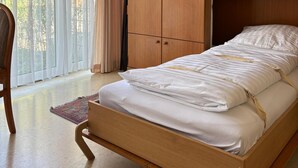 Ein Schlafzimmer mit einem hölzernen Bett, einem Kleiderschrank und einem Fenster mit durchsichtigen Vorhängen.