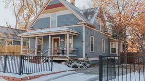 Une maison à deux étages avec un porche à l’avant, une cheminée et une cour enneigée.