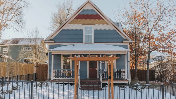 Une maison à deux étages avec un porche, une clôture en bois et une cour enneigée.