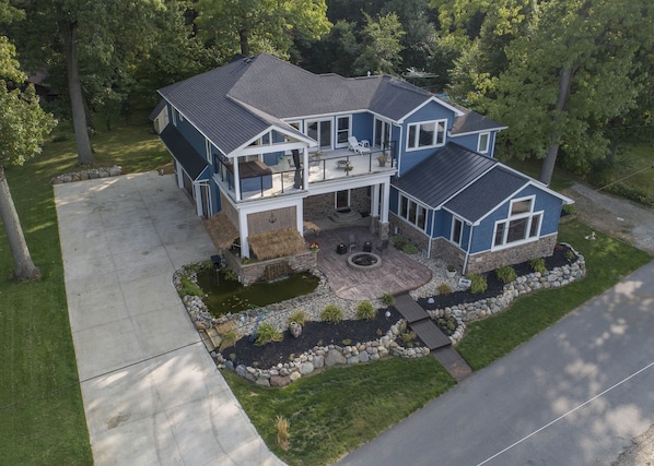 A two-story house with a patio, a fire pit, and a pond.