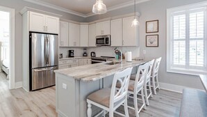A modern kitchen with white cabinets, stainless steel appliances, a marble island, and pendant lighting.