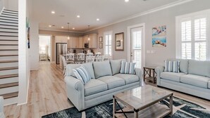 A spacious living room with a light blue sofa, a glass coffee table, and a dining area with white chairs.