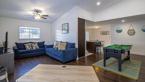 A living room with a blue sofa, a pool table, and a ceiling fan.