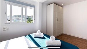 A modern bedroom with a bed, two towels, a wardrobe, and a window with a city view. - Pool Villa & Beach House (Torre de Benagalbón)