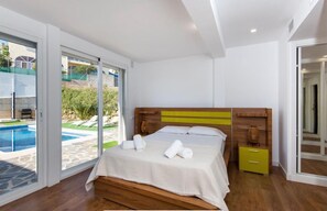 Un dormitorio con una cama grande, un cabecero de madera, una mesita de noche pequeña y vistas a una piscina.