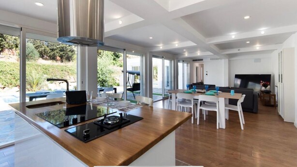 A modern kitchen with a central island, dining area with white chairs, and a living space with a sofa and TV. - Pool Villa & Beach House (Torre de Benagalbón)