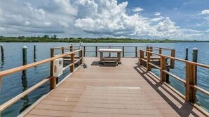 A wooden pier extending into calm water, with a bench and railing in the center. - Beautiful Barefoot Beach Resort Condo B207 on Boca Ciega Bay with beach access  (Indian Shores)