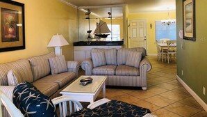 A living room with striped sofas, a coffee table, and a ceiling fan. - Beautiful Barefoot Beach Resort Condo B207 on Boca Ciega Bay with beach access  (Indian Shores)