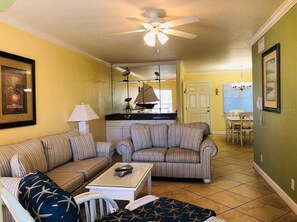 A living room with striped sofas, a coffee table, and a ceiling fan. - Beautiful Barefoot Beach Resort Condo B207 on Boca Ciega Bay with beach access  (Indian Shores)