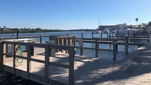 A wooden pier with a metal railing, leading to a marina with boats and a clear blue sky. - Beautiful Barefoot Beach Resort Condo B207 on Boca Ciega Bay with beach access  (Indian Shores)