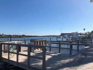 A wooden pier with a metal railing, leading to a marina with boats and a clear blue sky. - Beautiful Barefoot Beach Resort Condo B207 on Boca Ciega Bay with beach access  (Indian Shores)