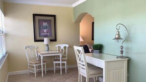 A dining area with a white table and chairs, a lamp, and a framed picture on the wall. - Beautiful Barefoot Beach Resort Condo B207 on Boca Ciega Bay with beach access  (Indian Shores)