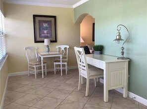 A dining area with a white table and chairs, a lamp, and a framed picture on the wall. - Beautiful Barefoot Beach Resort Condo B207 on Boca Ciega Bay with beach access  (Indian Shores)