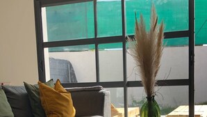 Un salon moderne avec un canapé gris, des coussins jaunes et verts, et une table basse en verre. Un vase vert contenant des plumes d'herbe des pampas est posé sur la table.