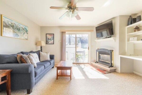 A living room with a grey sofa, a wooden coffee table, a fireplace, a ceiling fan, and a TV mounted on the wall. - ⛰️☀️ SKIING, HIKING, VILLAGE OF ELLICOTTVILLE MOUNTAIN ESCAPE (Ellicottville)