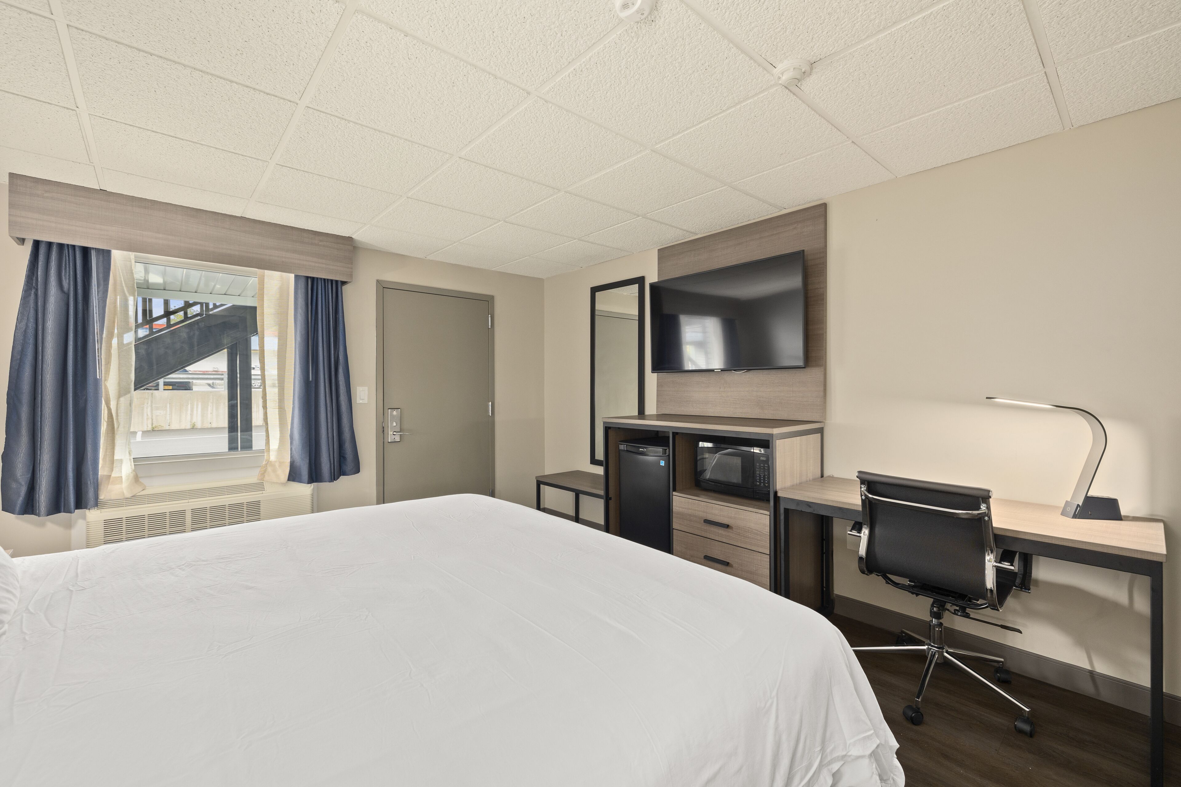 A hotel room with a large bed, a desk with a computer and a flat-screen TV, a microwave, and a small kitchenette.