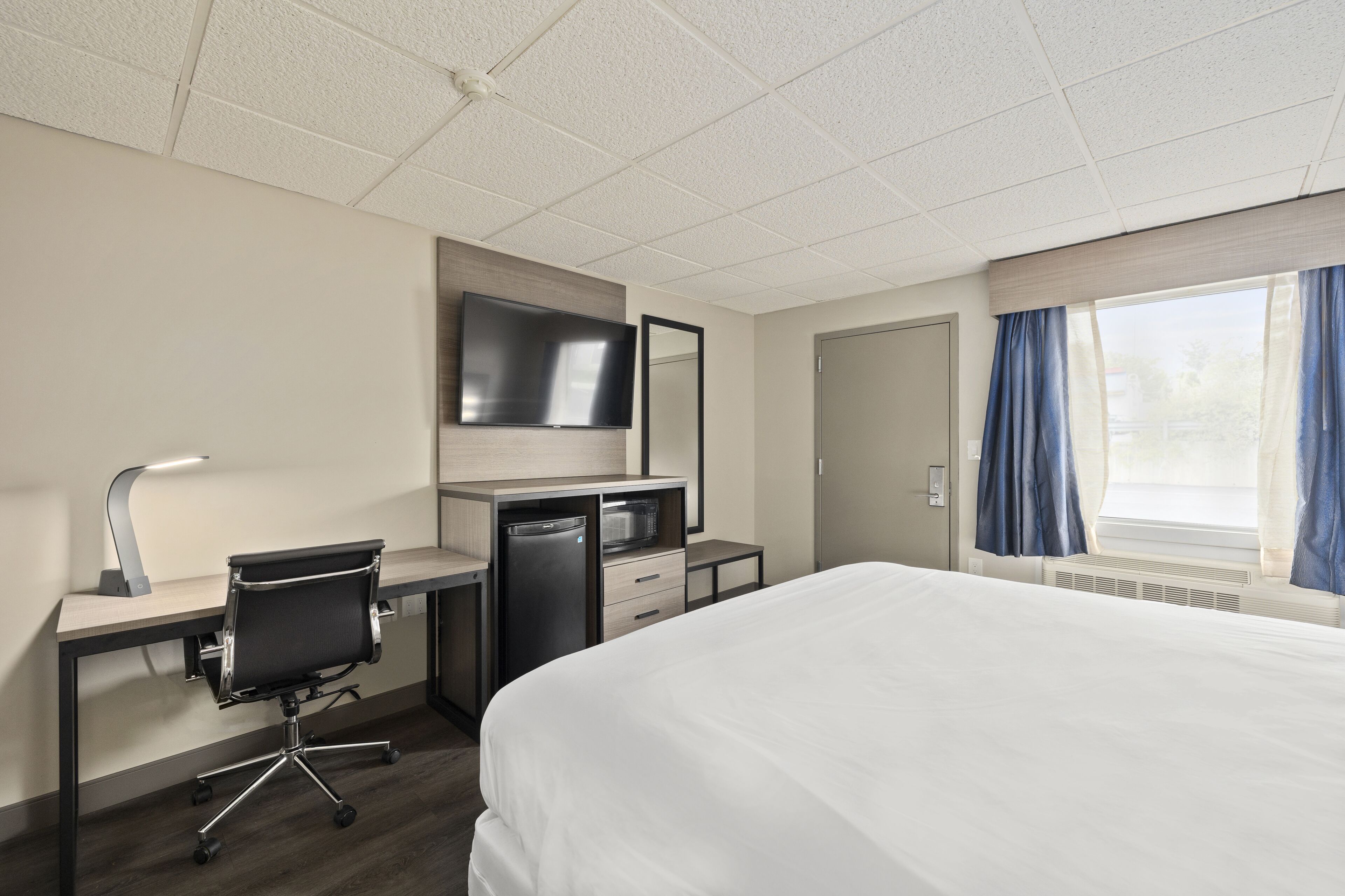 A hotel room with a bed, desk, chair, TV, and a window with curtains.