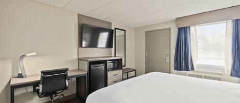 A hotel room with a bed, desk, chair, TV, and a window with curtains.