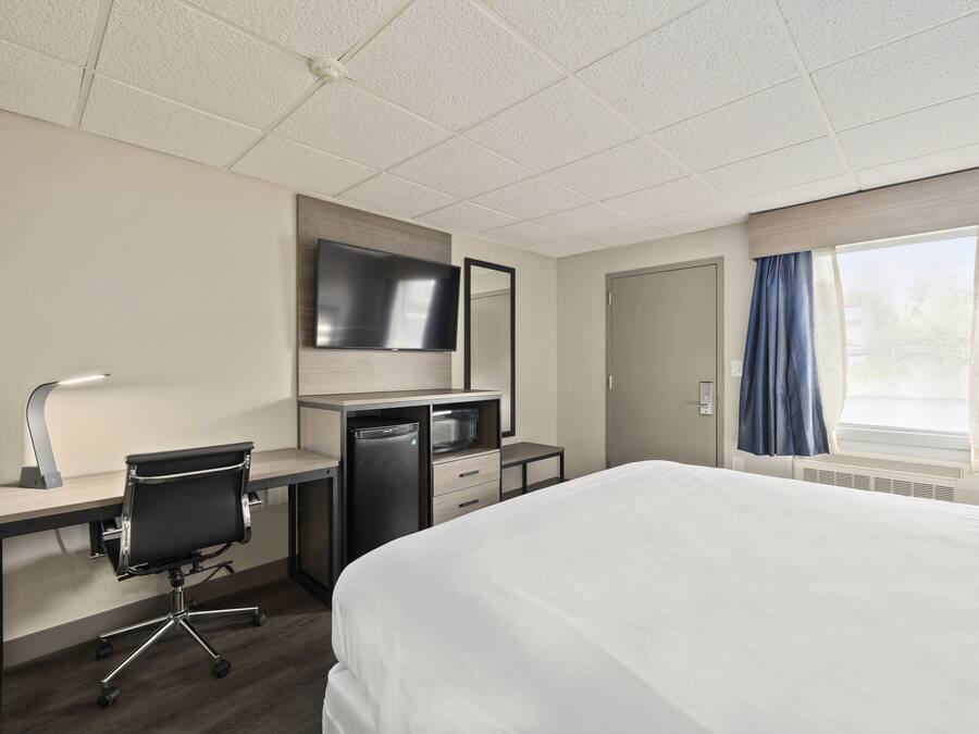 Habitación de hotel con cama, escritorio, silla, televisor y ventana con cortinas.