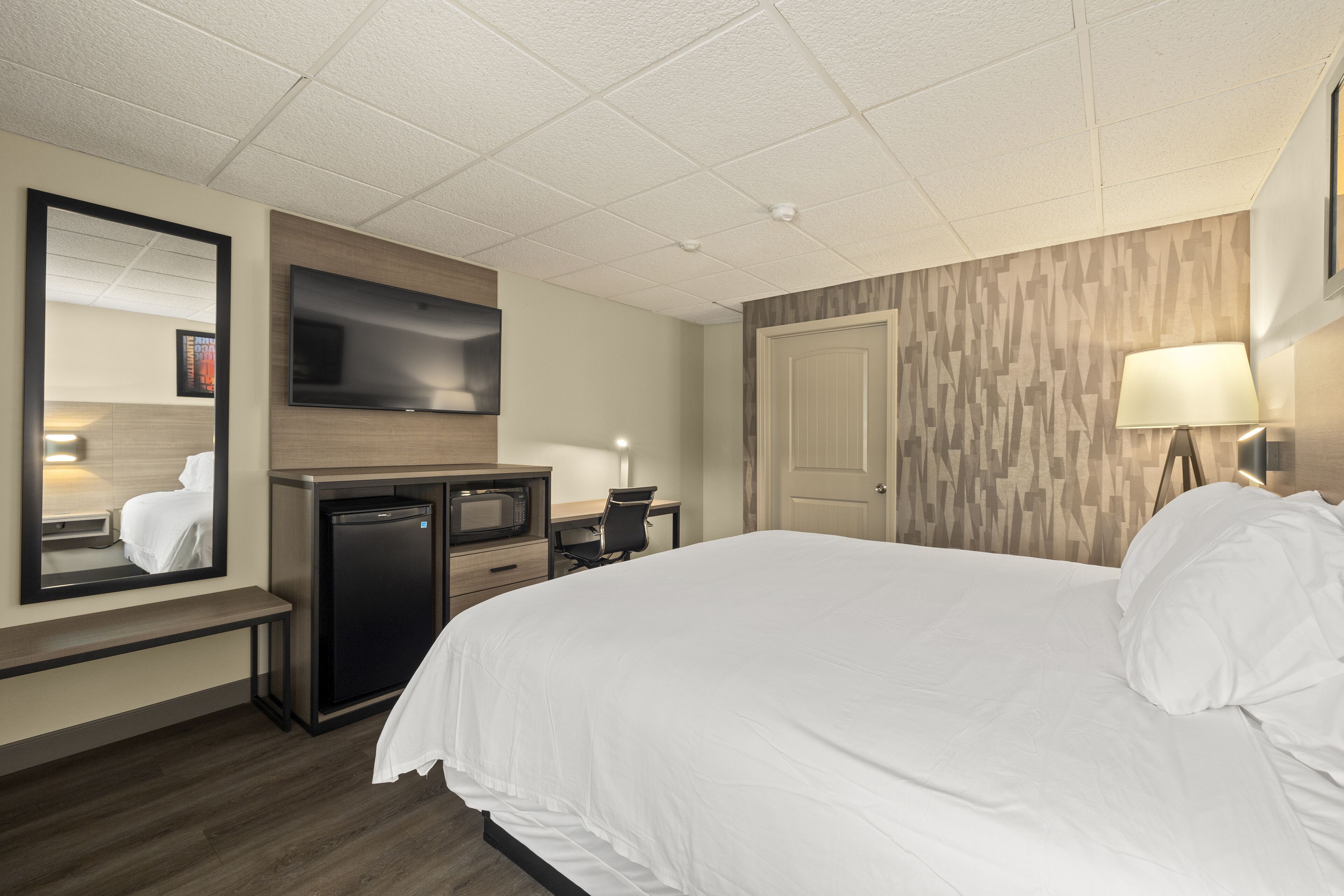 A hotel room with a bed, a desk, a television, a mirror, and a door.