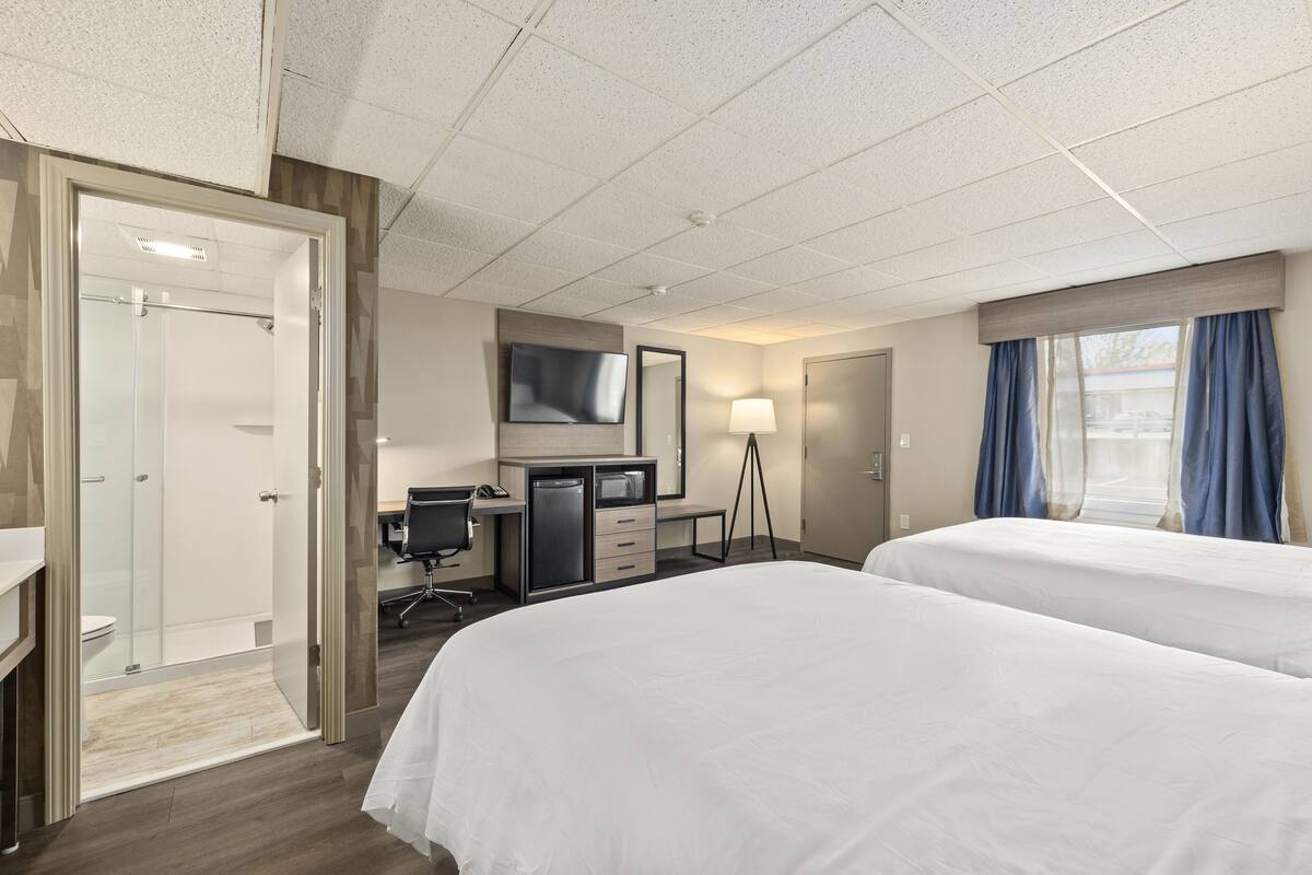 A hotel room with two beds, a desk, a television, and a bathroom.