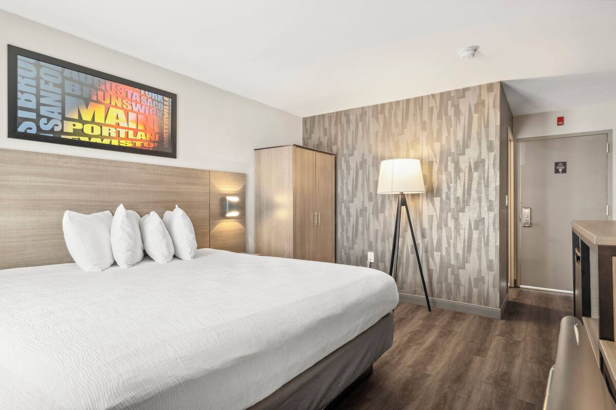 A hotel room with a large bed, a wardrobe, a desk, and a wall-mounted lamp.