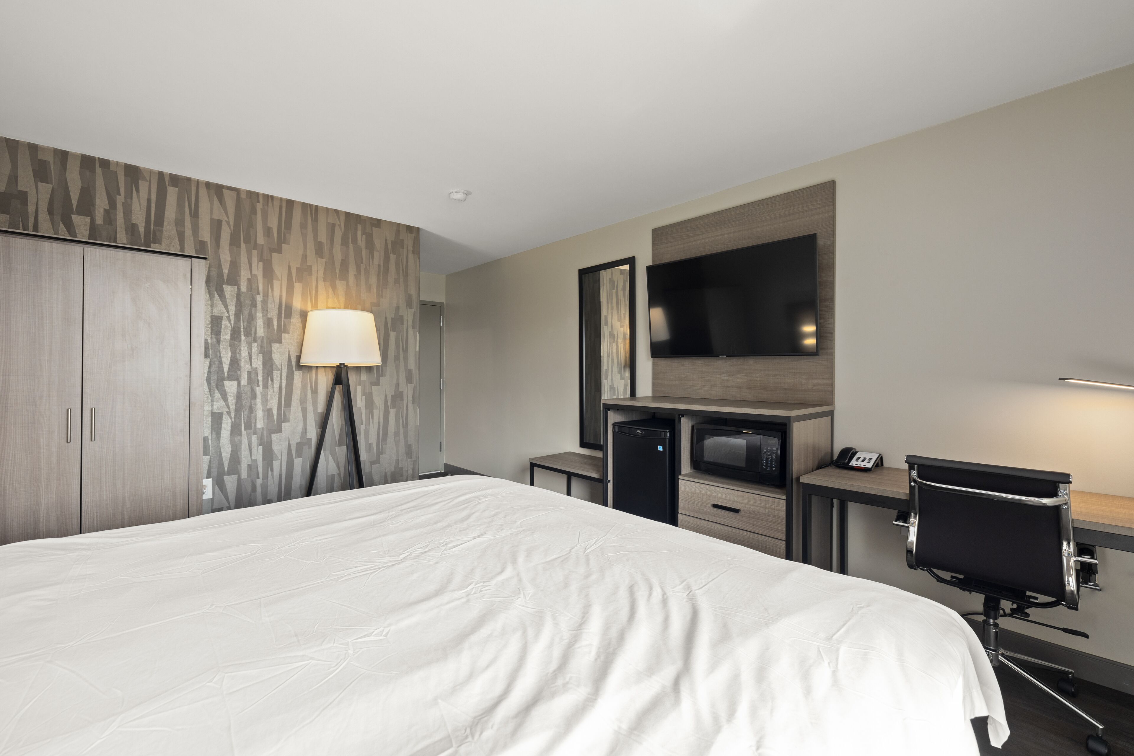 A hotel room with a large bed, a desk with a chair, a television, and a wardrobe.