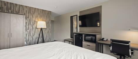A hotel room with a large bed, a desk with a chair, a television, and a wardrobe.