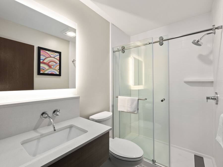Een moderne badkamer met een douchecabine van glas, een witte wastafel en een toilet.